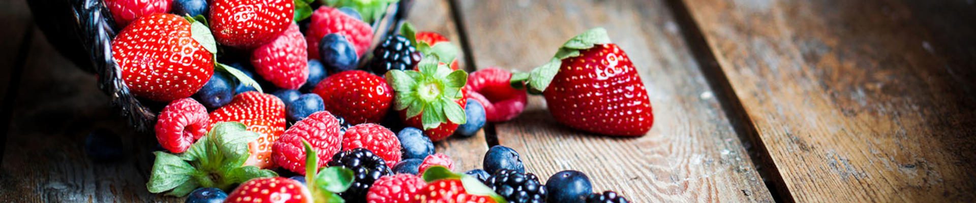 Mix of fresh berries in a basket on rustic wooden background